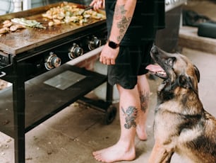 um homem ao lado de um cachorro em frente a uma churrasqueira