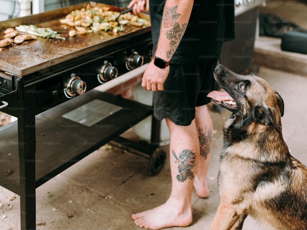 a man standing next to a dog in front of a grill