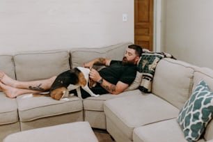 a man laying on top of a couch next to a dog