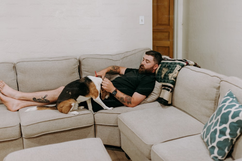 Un hombre acostado encima de un sofá junto a un perro