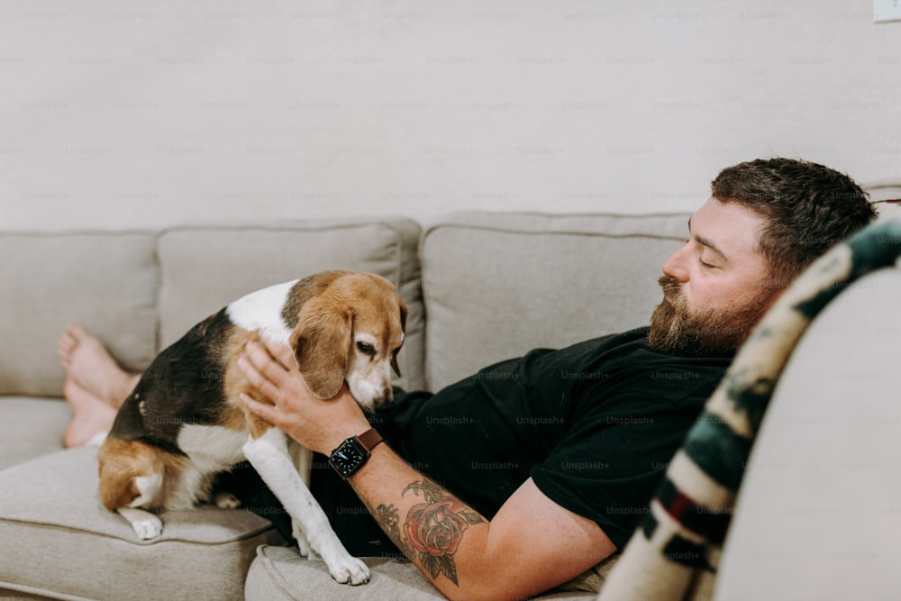 a man sitting on a couch petting a dog