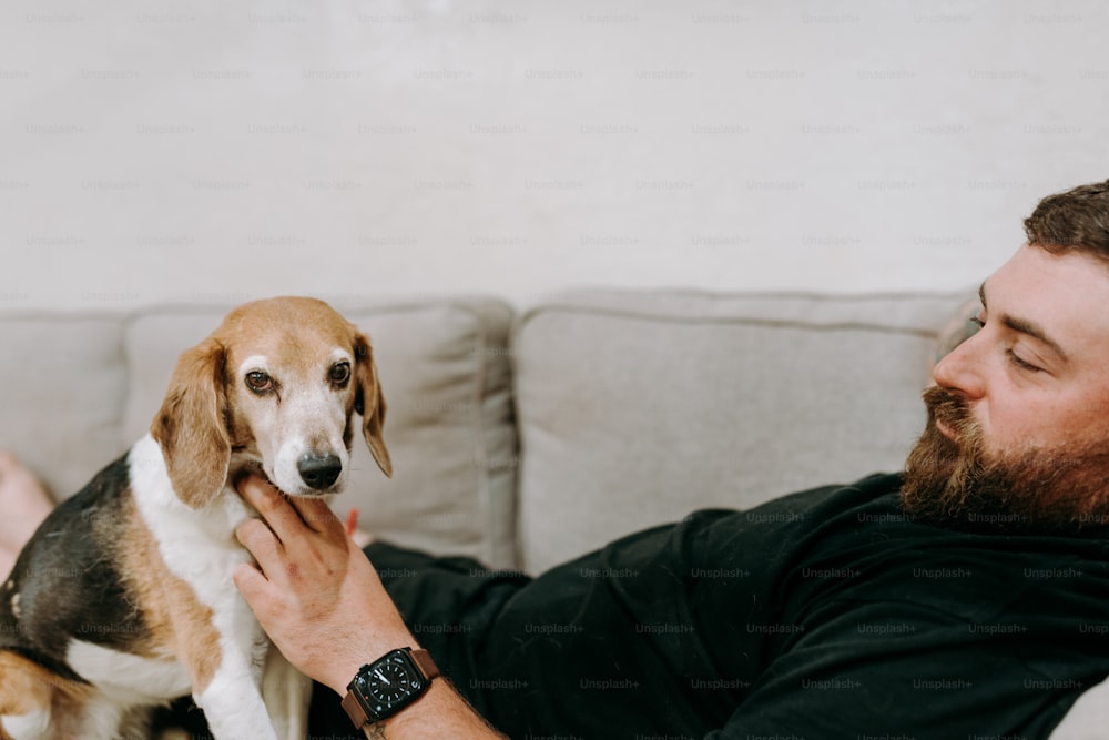 a man sitting on a couch petting a dog