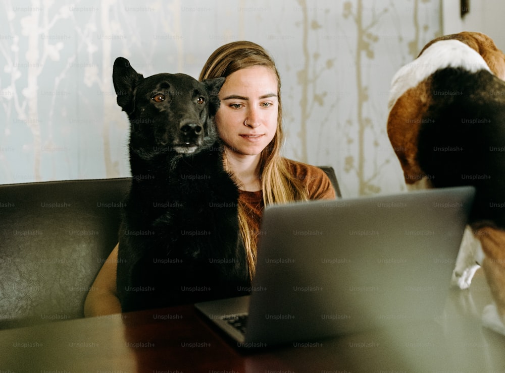 a woman sitting at a table with a laptop and a dog