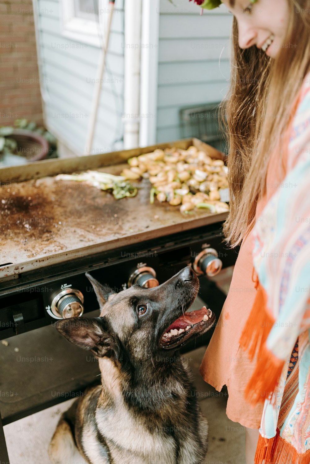 a woman standing next to a dog in front of a grill