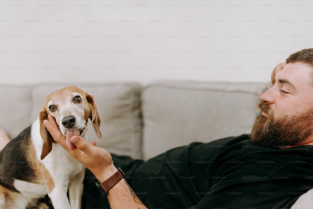 Un hombre acostado en un sofá acariciando a un perro