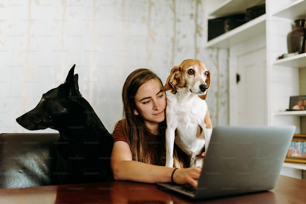 Une femme assise à une table avec un ordinateur portable et un chien sur ses genoux