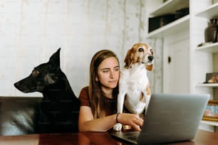 a woman sitting at a table with a dog and a laptop