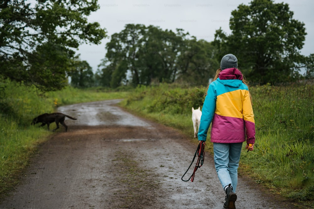 a woman walking down a dirt road with a dog