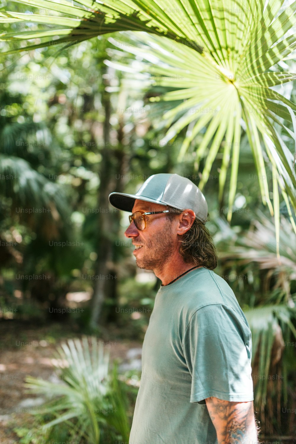a man wearing a hat and sunglasses standing in a forest