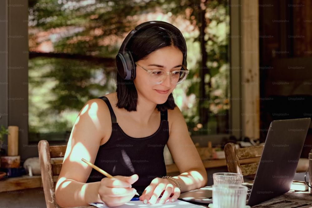 Una donna seduta a un tavolo con un computer portatile e cuffie accese