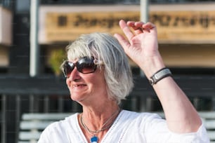 a woman with white hair and sunglasses holding her hand up in the air