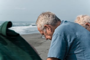an older man looking at something in a bag on the beach
