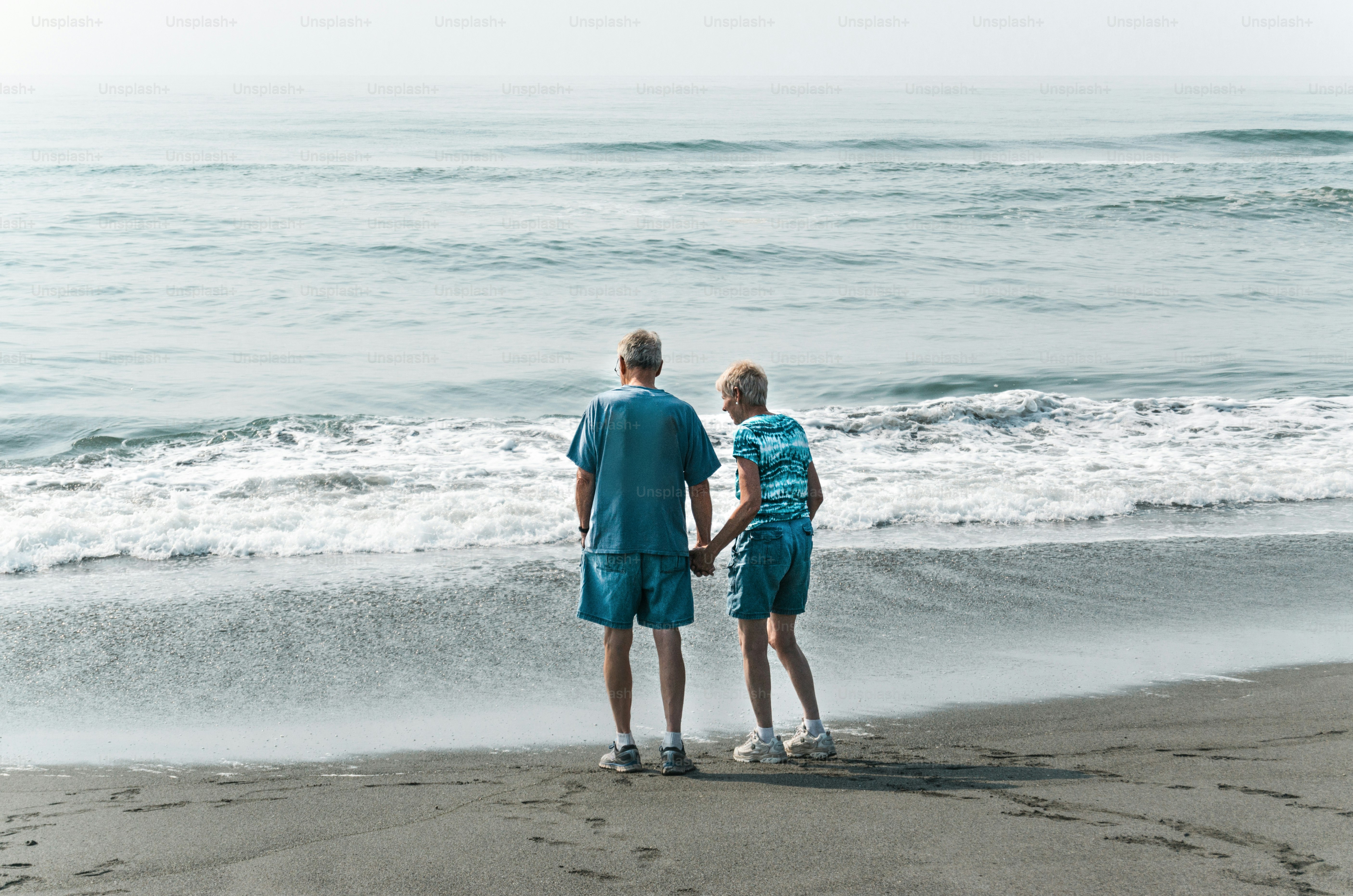 A man and woman standing on a beach next to the ocean photo – Beach ...