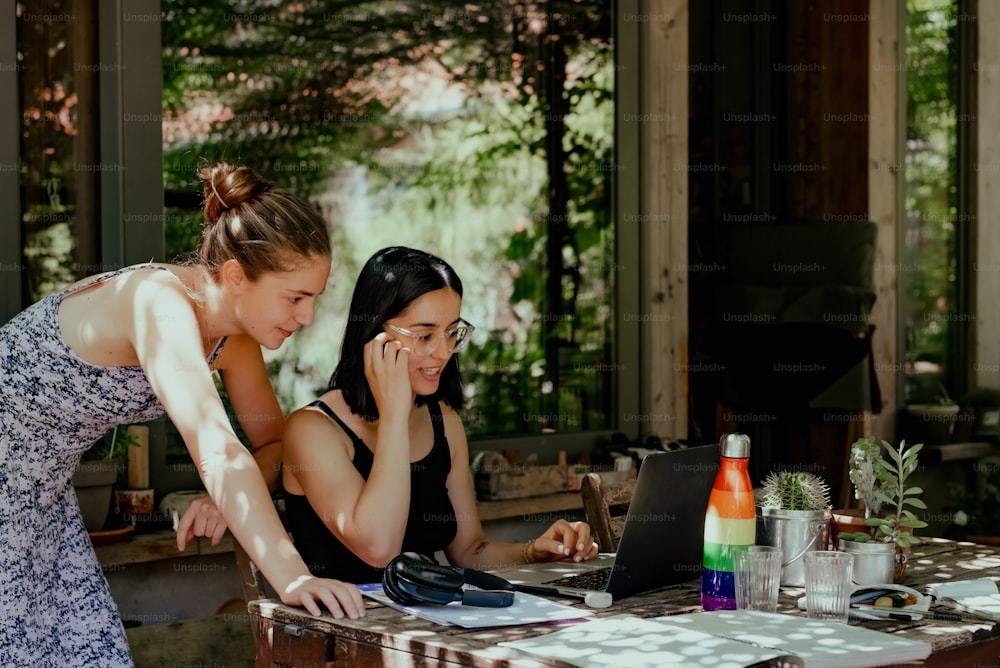 two women sitting at a table with a laptop