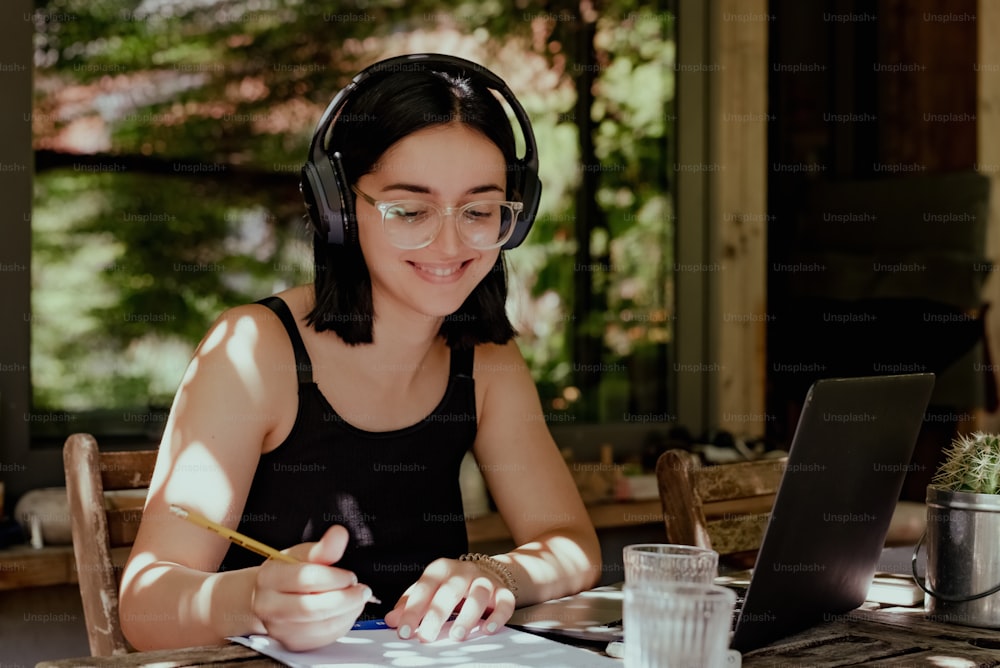 Una donna seduta a un tavolo con un computer portatile e cuffie accese