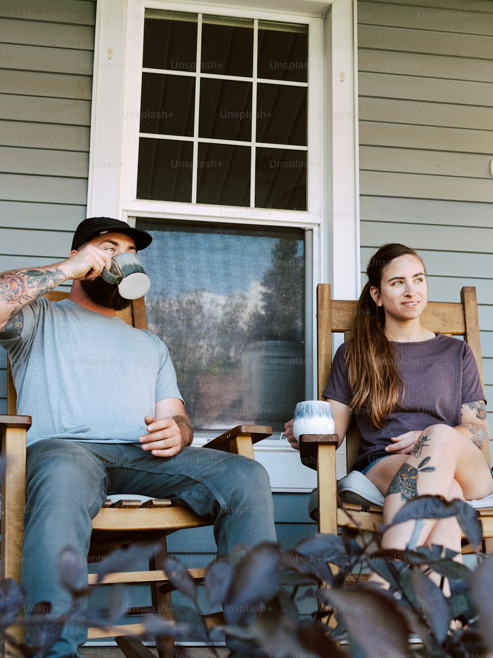 a man and a woman sitting on rocking chairs outside of a house