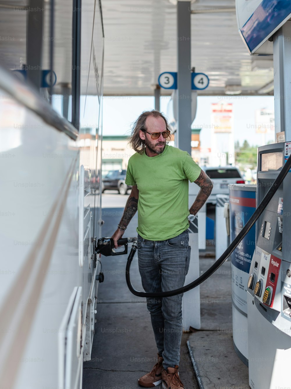 a man in a green shirt is pumping gas into his car