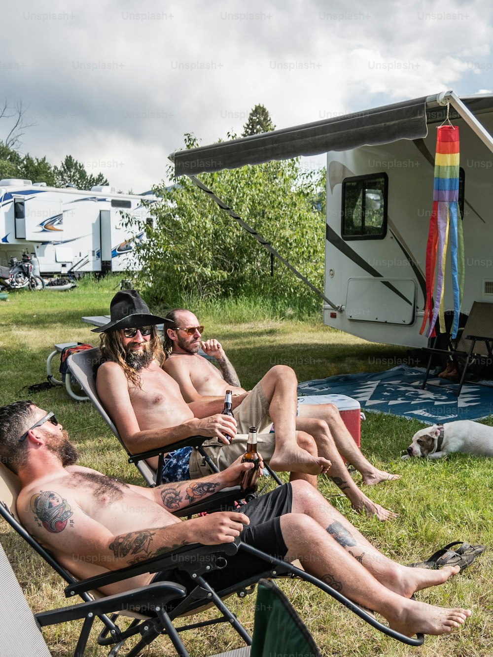 a group of men sitting in lawn chairs in front of a camper
