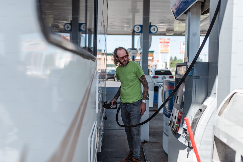 a man in a green shirt pumping gas into his car