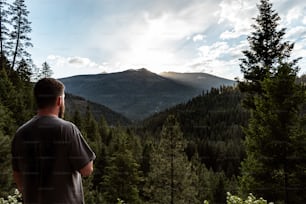 um homem parado em frente a uma floresta olhando para uma montanha