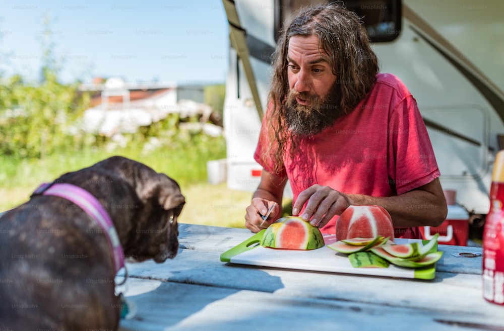 a man is cutting watermelon on a picnic table