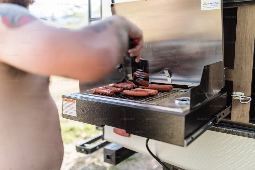 a man is cooking hot dogs on a grill