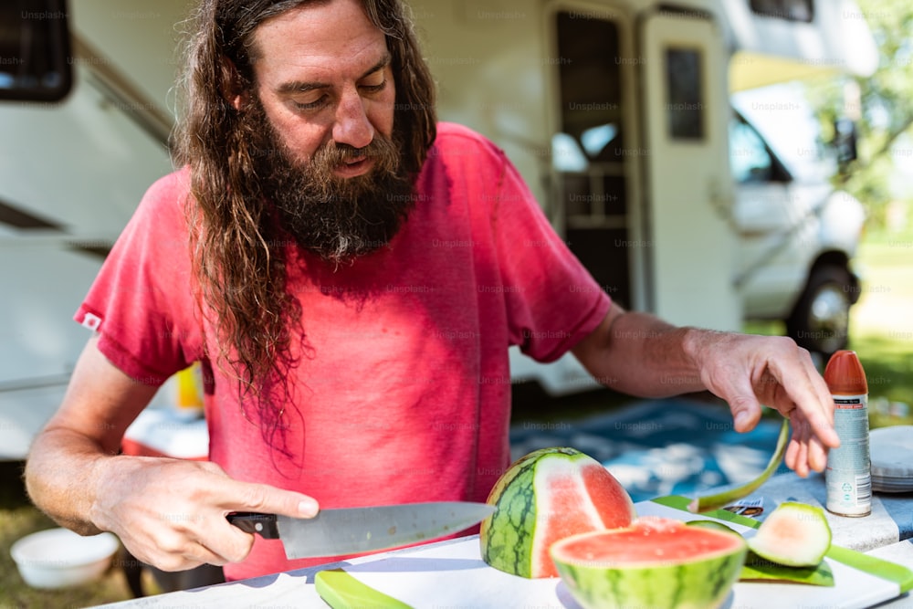 a man cutting a watermelon slice with a knife