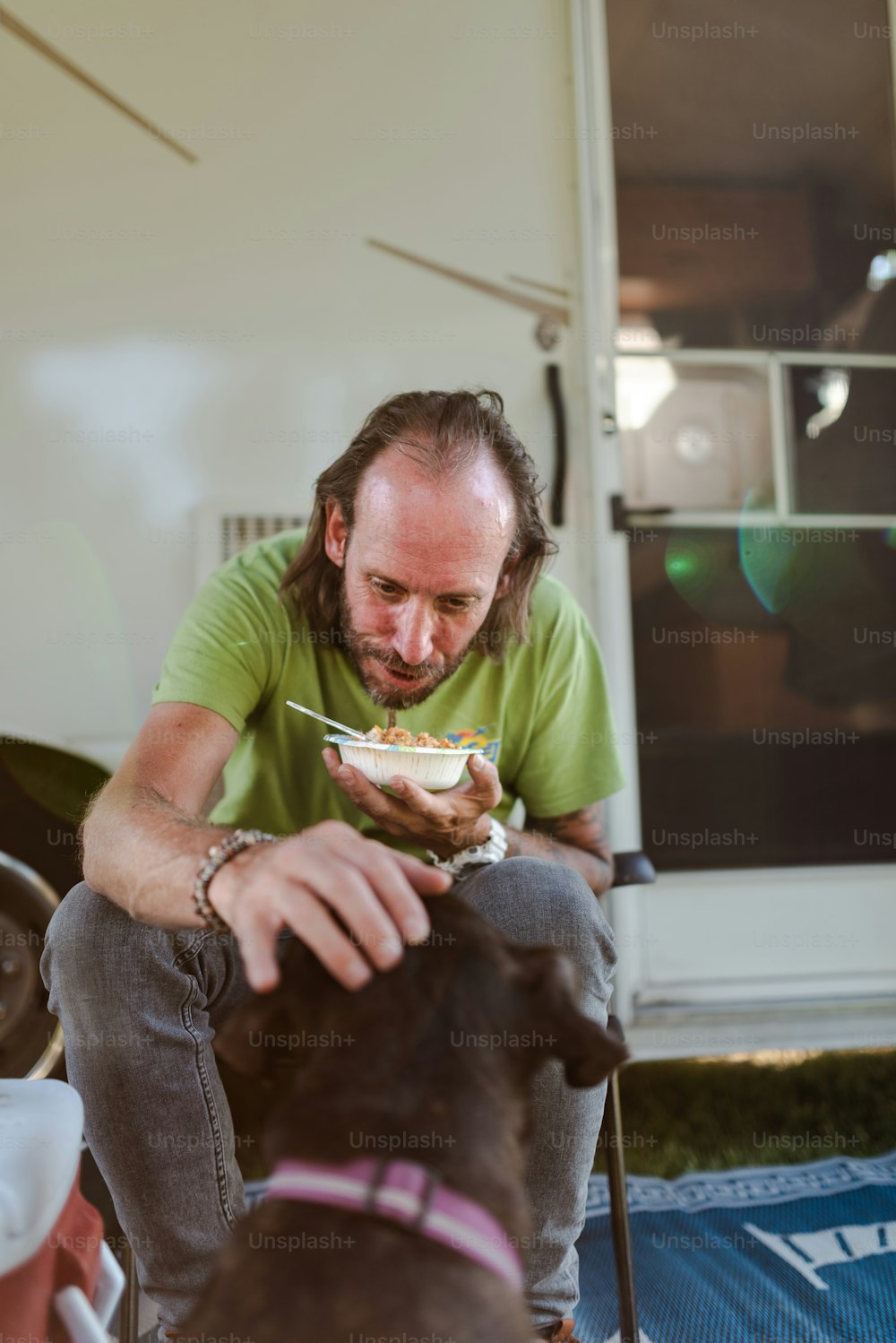 a man sitting on the ground with a bowl of food in front of his dog