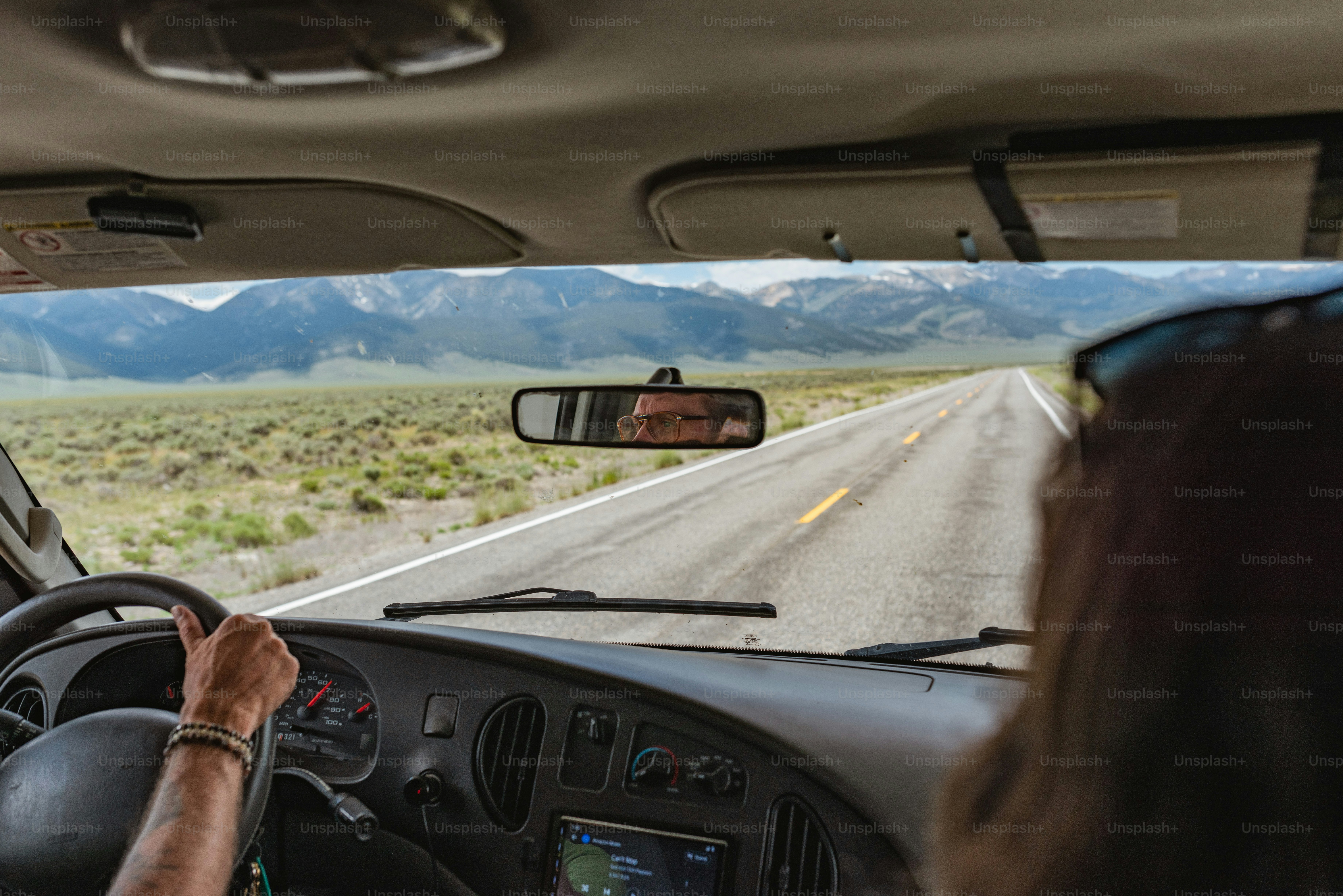 a woman driving a car on a road with mountains in the background