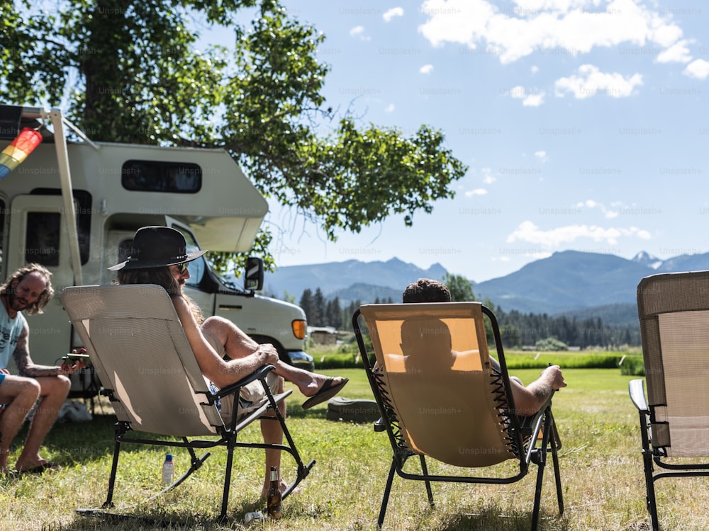 a couple of people sitting in lawn chairs in front of a camper