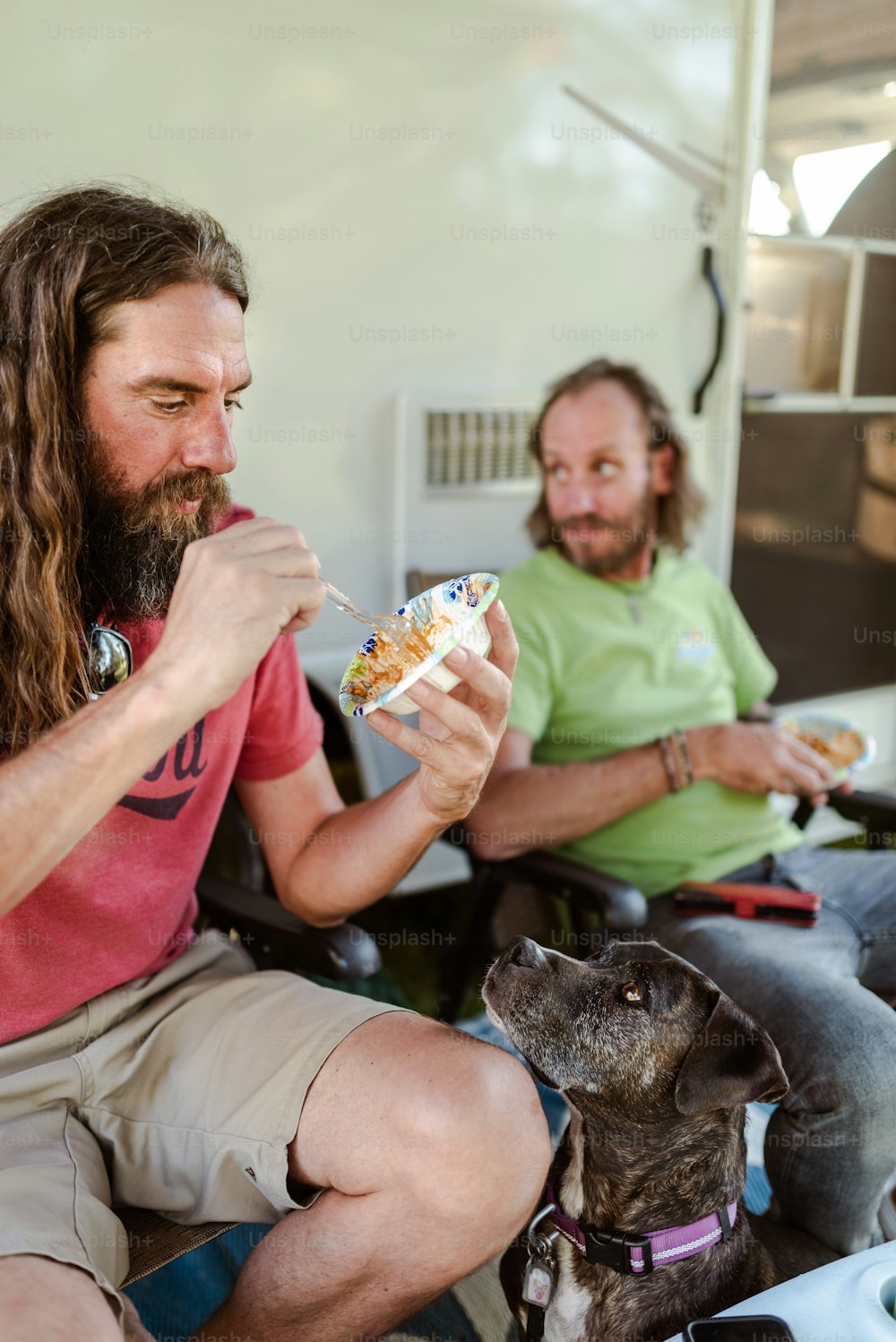 a man with long hair and a beard eating food next to a dog