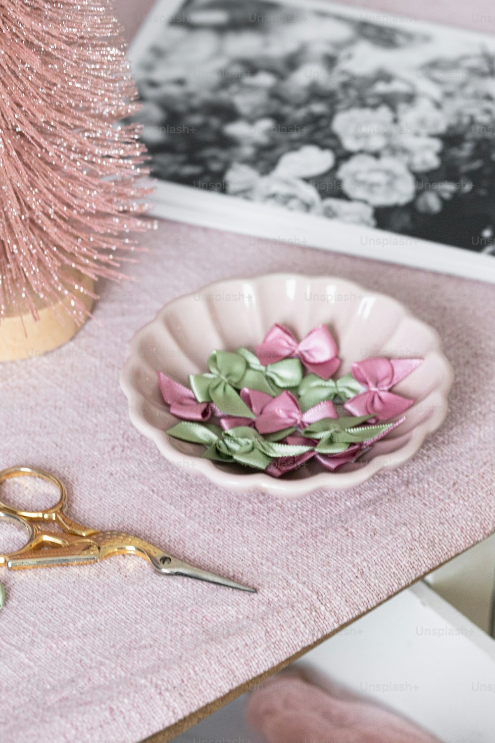 a pink table topped with a bowl of flowers and a pair of scissors