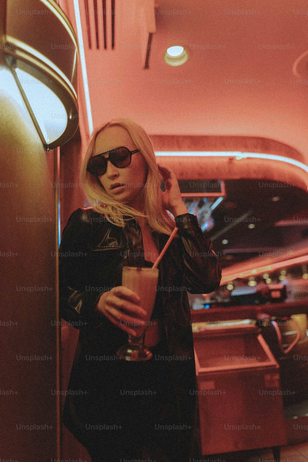a woman in a black jacket and sunglasses holding a drink