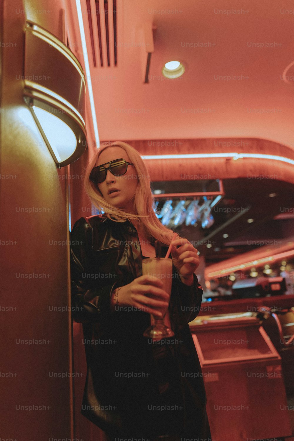 a woman in a leather jacket and sunglasses holding a drink