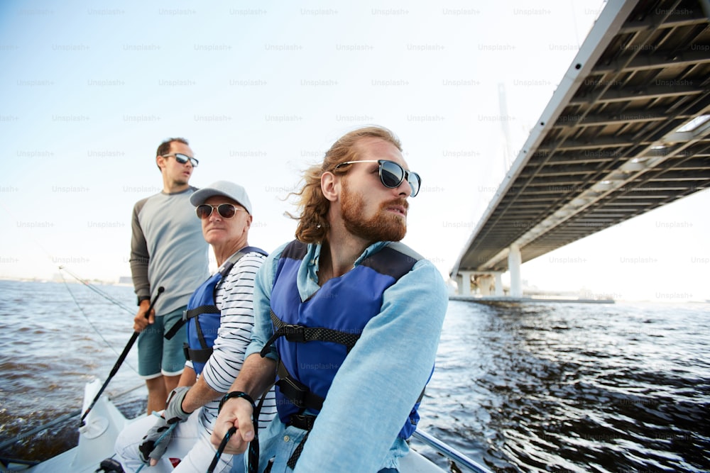 Des hommes pensifs et rêveurs d’âges différents naviguent ensemble sur un yacht et s’amusent à flotter sur la rivière, ils regardent autour d’eux