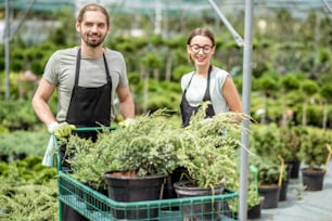 温室の緑の植物でいっぱいのショッピングカートを持つ制服を着た労働者の肖像画