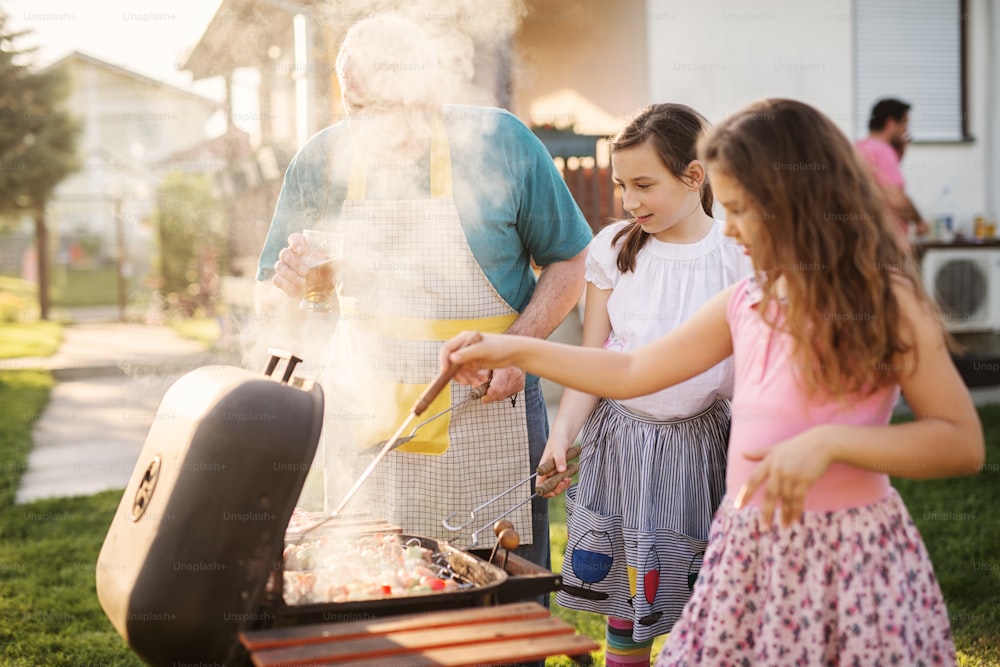 Happy grandfather is teaching his beautiful granddaughters how to make barbeque.