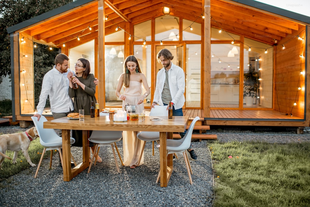 Cuatro amigos disfrutando de la noche cenando en el patio trasero de la moderna casa de campo al aire libre
