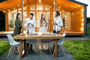 Friends having a dinner with pizza on the backyard of the modern house decorated with lights during the evening time outdoors