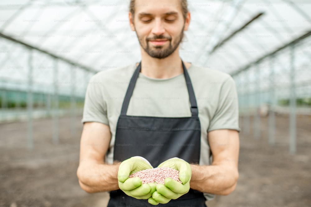 Farmer holding mineral fertilizers in the glasshouse with cultivated soil ready for fertilization