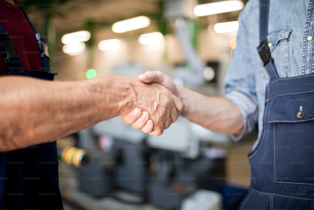 Close-up of two workers shaking hands with each other at the industrial factory