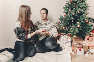 merry christmas and happy new year concept. stylish hipster couple exchanging with gifts in festive room under christmas tree with lights, space for text. happy holidays. family atmospheric moments