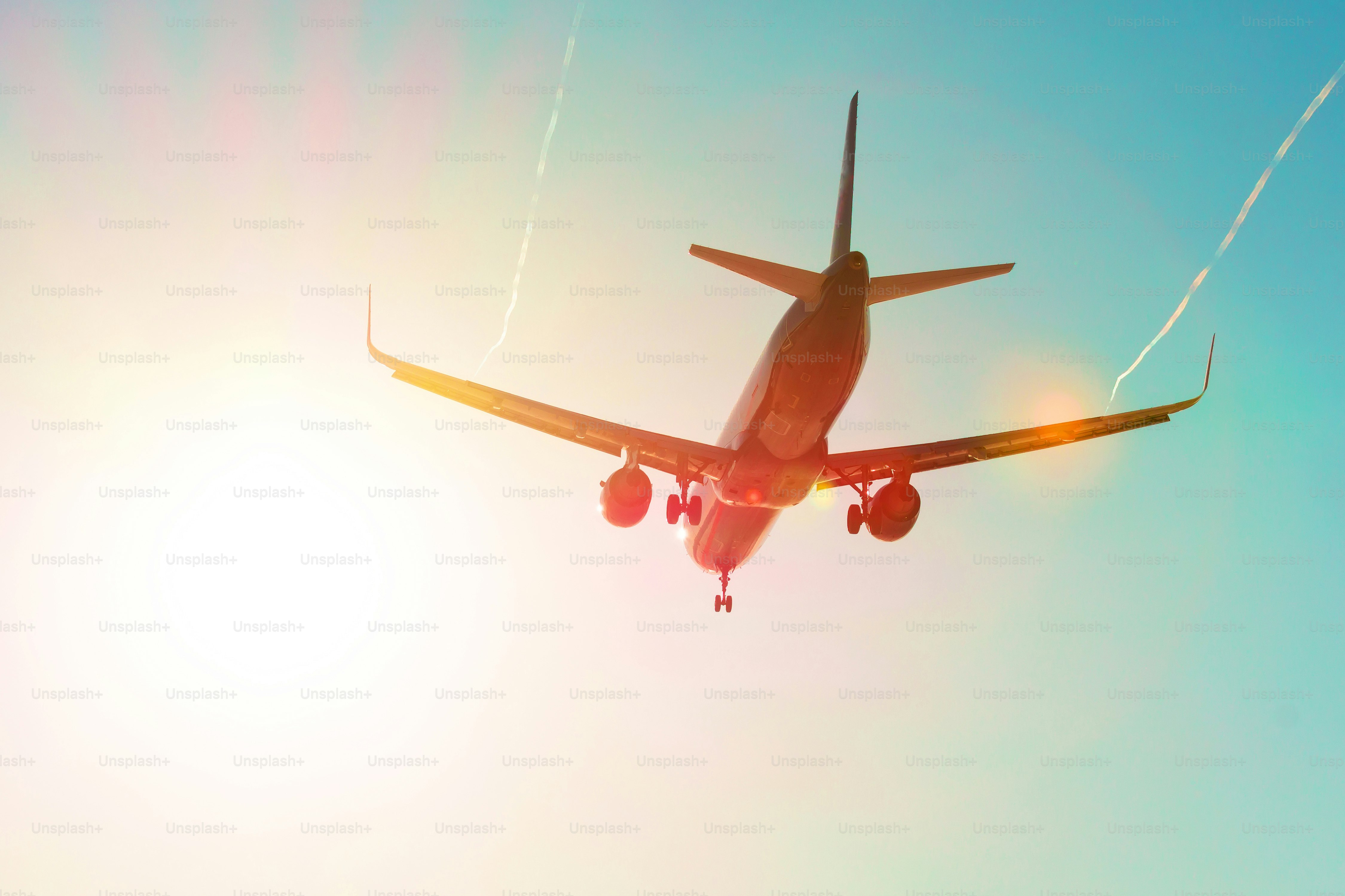 Passenger airplane flies near the sun glare with a color rainbow gradient on landing, with the wings of a steam jet vortex