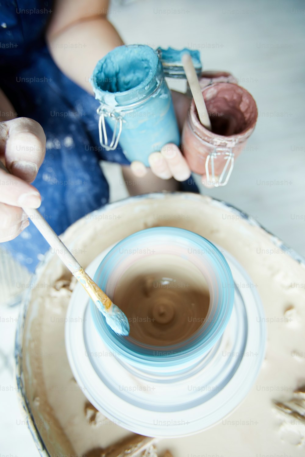 Pennello con colore blu in mano del vasaio creativo sopra la brocca rotante nella ruota di ceramica