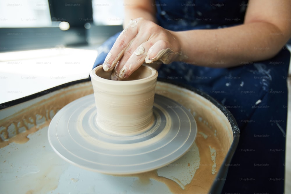 Manos del alfarero durante el proceso de fabricación de vasijas y jarras de barro en torno de alfarería en el taller