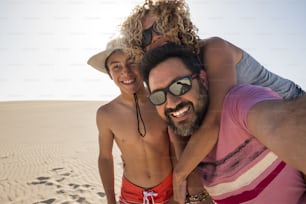happy family taking selfie picture on vacation during the summer holiday at the beach. Fuerteventura desert and three caucasian people having fun and joy together. love and relationship. travel and smile concept