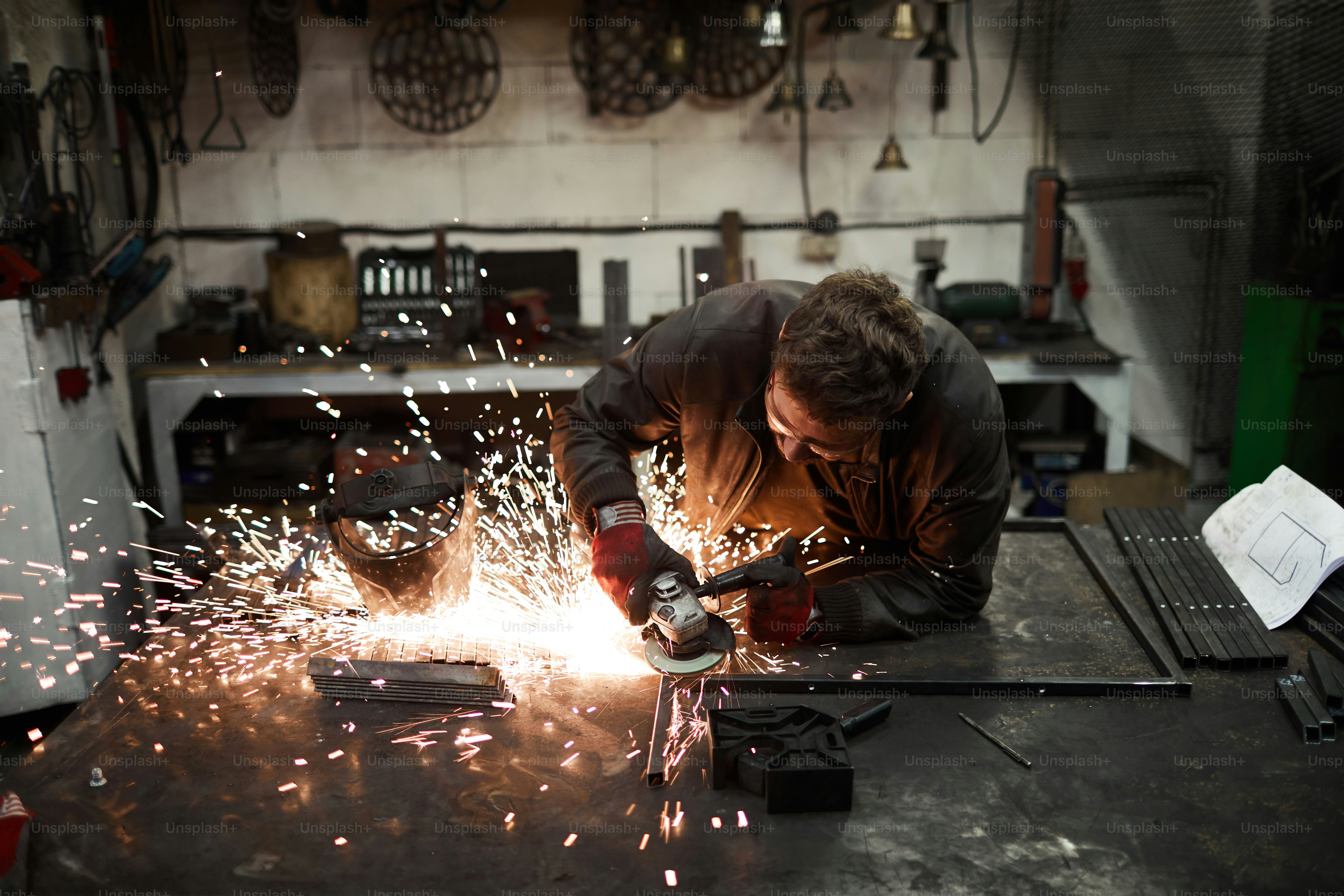 Young contemporary blacksmith standing by iron anvil and processing