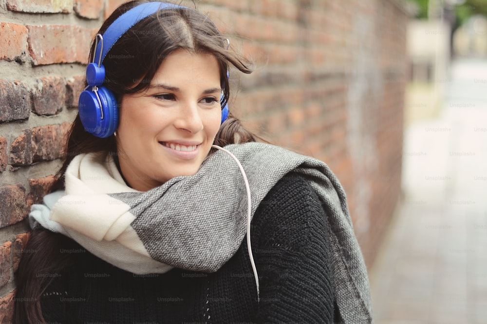 Portrait of young latin woman with blue headphones against a wall.