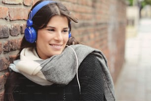 Portrait of young latin woman with blue headphones against a wall.