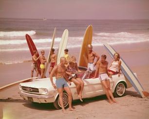 Un groupe de surfeurs sur une plage avec une Ford Mustang.